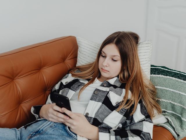 Jente i sofaen som sitter på mobiltelefonen